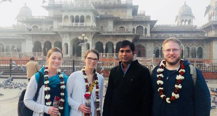 Quatre personnes avec des guirlandes devant un monument architectural.