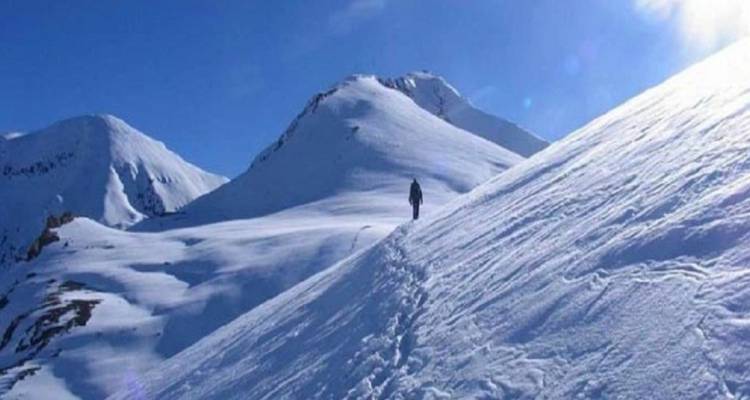 Eenzame figuur die door besneeuwde bergachtige omgeving trekt.