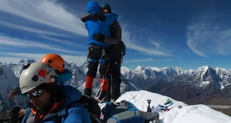 Bergbeklimmers die feest vieren op een besneeuwde bergtop met uitzicht over een uitgestrekt berglandschap.