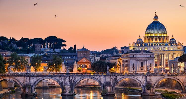 La Basílica de San Pedro y el puente del río Tíber brillan al atardecer en Roma.