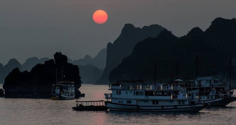Boten op het water tijdens een schilderachtige zonsondergang in een baai omringd door rotsachtige eilandjes.