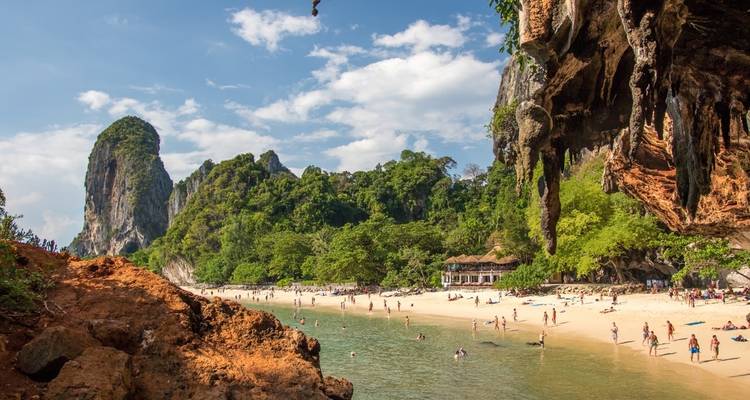 Toeristen die genieten van een zandstrand met kalkstenen kliffen onder een zonnige hemel.