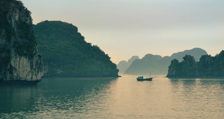 Mistige en serene baai met een eenzame boot en hoge kalksteenformaties.