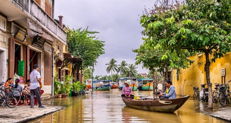 Overstroomde straat met mensen die boten gebruiken tussen kleurrijke gebouwen.