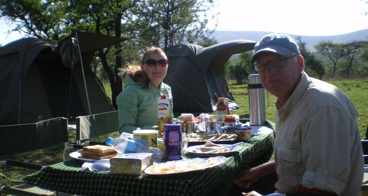 Ein Paar, das an einem Tisch mit Essen in einem Safari-Campingplatz sitzt.
