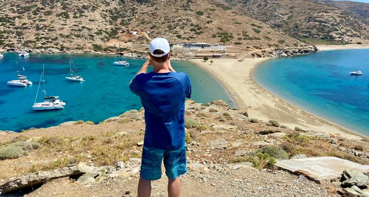 Een man die een foto maakt van een strand met zeilboten in helder blauw water.