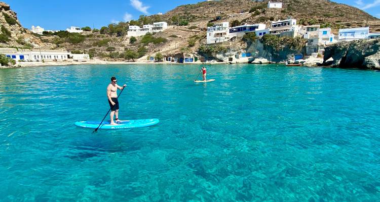 Twee mensen die aan het paddleboarden zijn op helder blauw water voor een rotsachtige kust.
