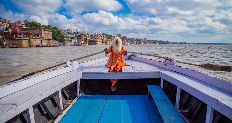 A spiritual person sits relaxed on a boat in Varanasi, against the backdrop of city ghats.