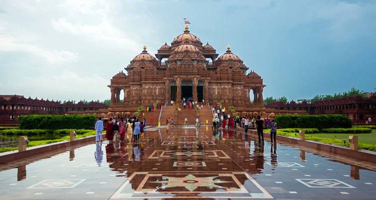 Akshardham Temple with visitors reflected in standing water.