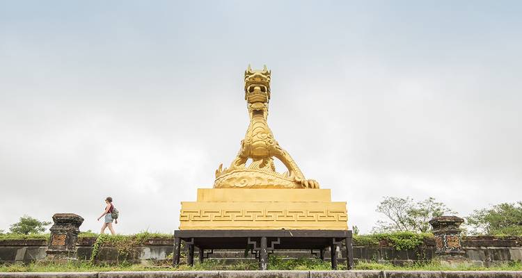 Une personne marchant près d'une statue culturelle dorée par une journée nuageuse.