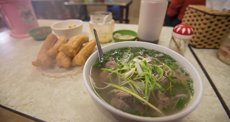 Un bol de soupe avec des nouilles et des légumes verts dans un cadre décontracté.