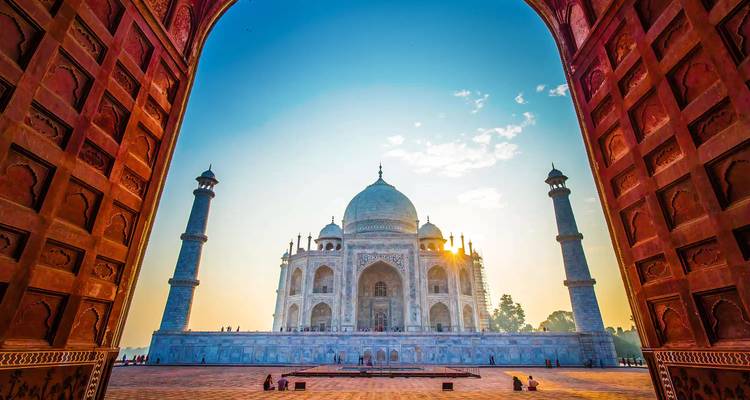 The Taj Mahal viewed from an arched entrance, with a sunlit backdrop.