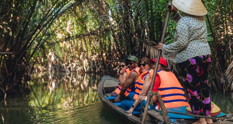 Los viajeros con chalecos salvavidas naranjas se deslizan en bote por los estrechos y sombreados canales del Mekong repletos de palmeras.