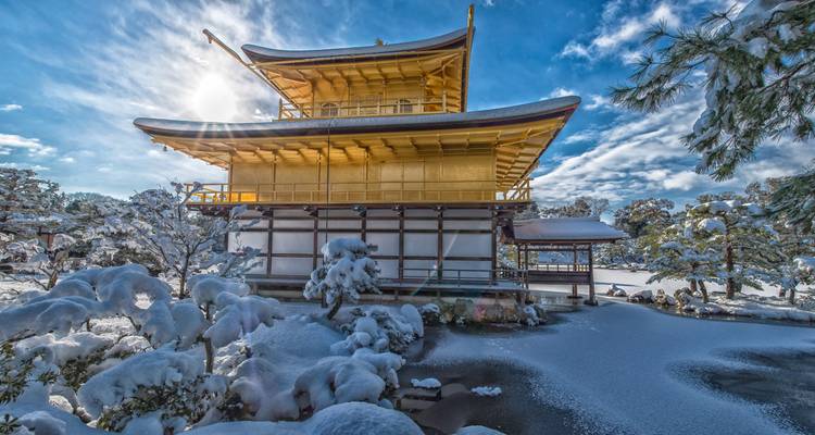 Pabellón Dorado de Kinkaku-ji reluciendo contra un cielo invernal brillante sobre jardines cargados de nieve.