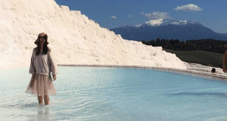 Person wading in the travertine pools with mountains in the background.