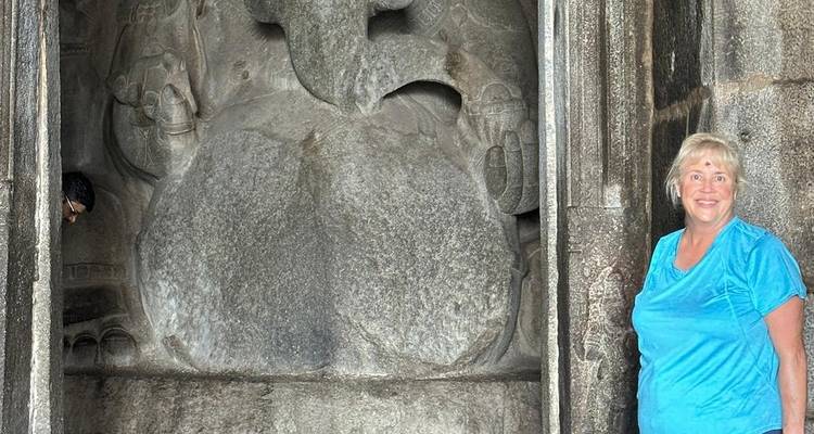 Vrouw die naast een kolossaal oud beeldhouwwerk staat.