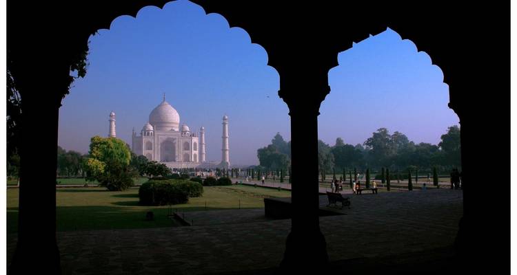 Taj Mahal omlijst door een donkere boog onder een blauwe hemel.
