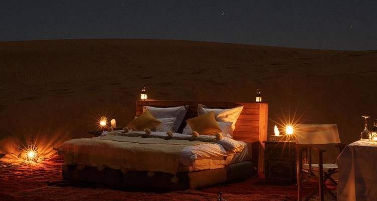 Woestijnkampeerplaats met een bed en lantaarns 's nachts.