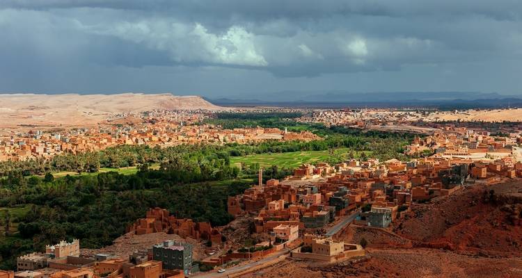 Expansive view of a valley with buildings and greenery, under a cloudy sky.