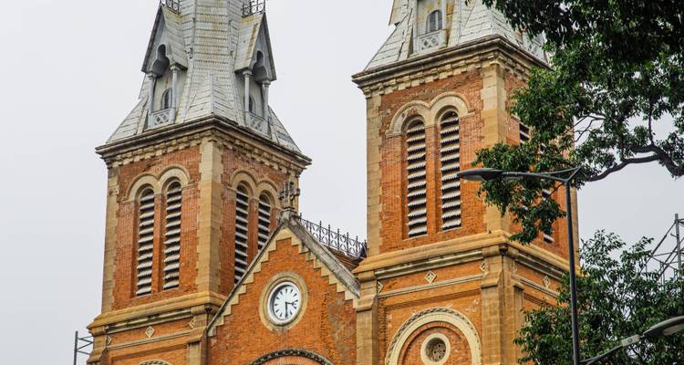 Zwillingsglockentürme der roten Ziegelstein-Kathedrale Notre Dame Basilika von Saigon, die sich gegen einen bewölkten Himmel erheben.