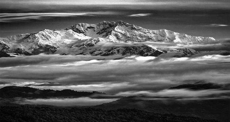 Een dramatische zwart-witfoto van een bergtop omringd door wolken.
