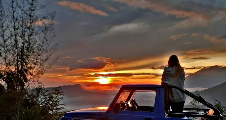 Person standing on a vehicle watching the sunrise over misty hills.