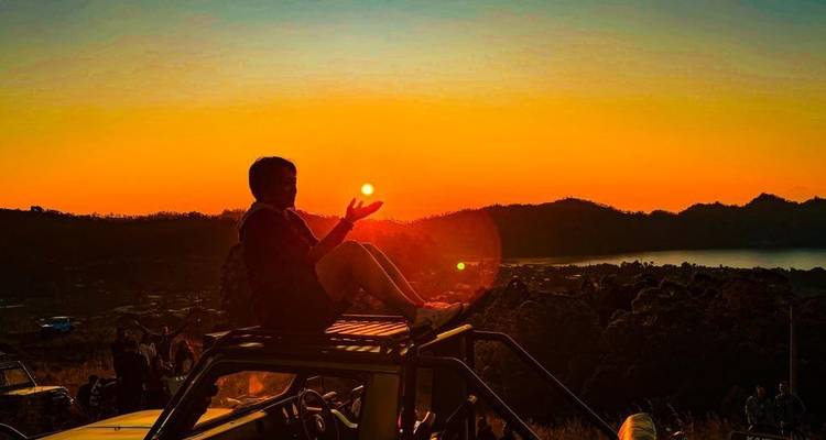 Silhouette of a person on a vehicle rooftop holding the sun at sunset.