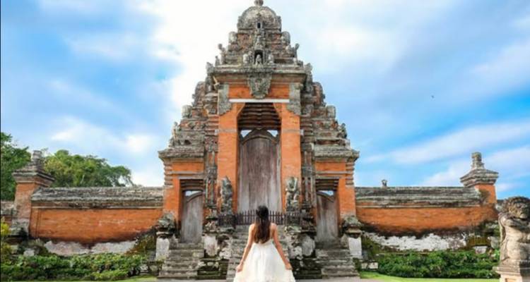Person walking towards a traditional temple gate under a blue sky.