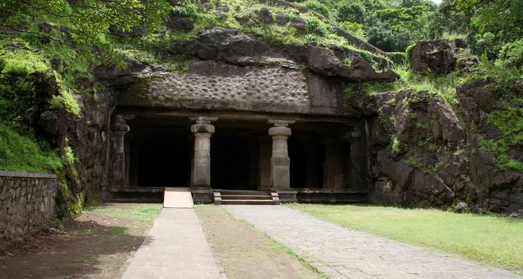 Cave entrance in a rock face surrounded by greenery.