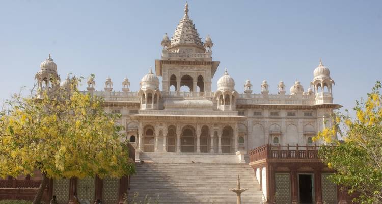 A grand white marble mausoleum with intricate domes surrounded by lush greenery.