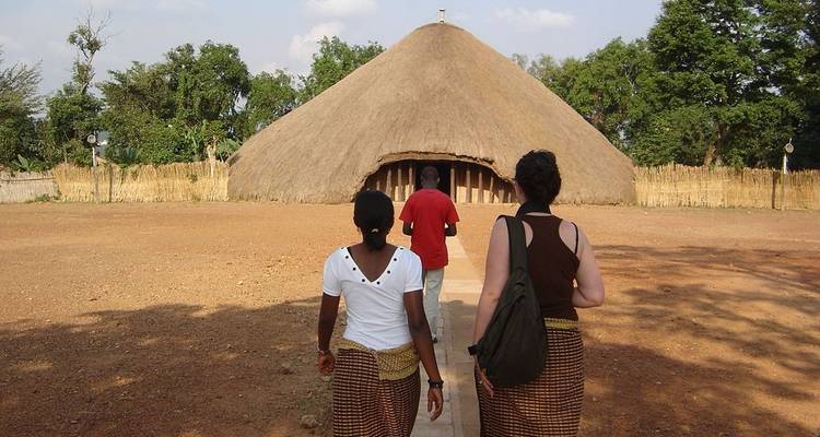Drei Personen gehen auf eine traditionelle Hütte zu.