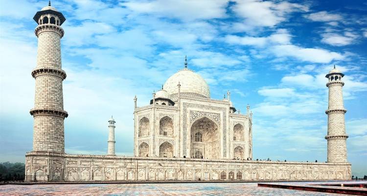Zijprofiel van de Taj Mahal met twee uittorenende minaretten tegen een levendige blauwe lucht.