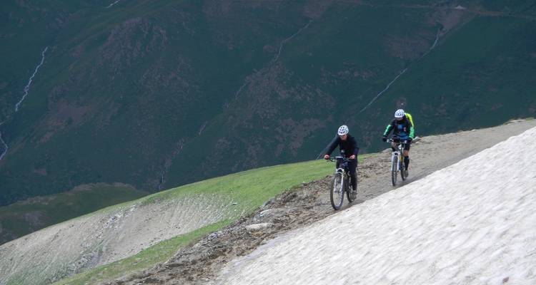 Deux cyclistes roulent le long d'un sentier de montagne bordé de neige au-dessus de pentes abruptes.