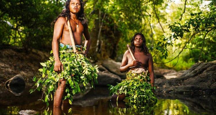 Twee mannen die in een beek staan en bladachtige kleding dragen.