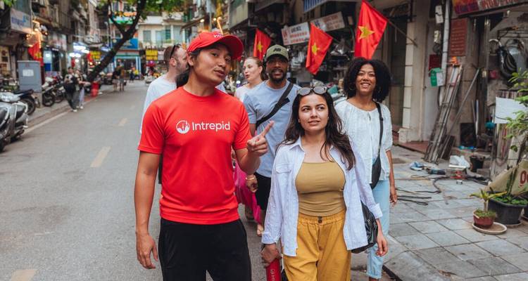 Le guide explique les curiosités locales à un petit groupe en descendant une rue de Hanoi bordée de drapeaux.