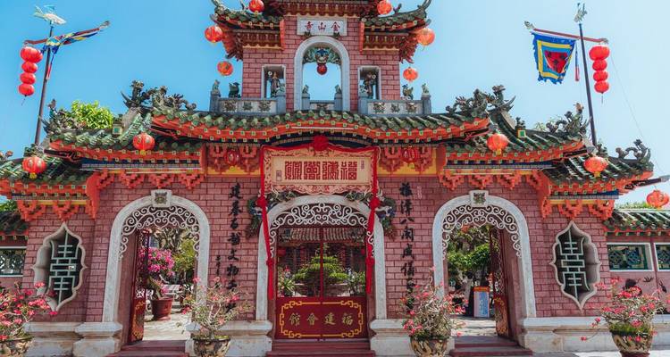 Salle d'assemblée de style chinois orné avec briques rouges, dragons et lanternes sous un ciel dégagé.