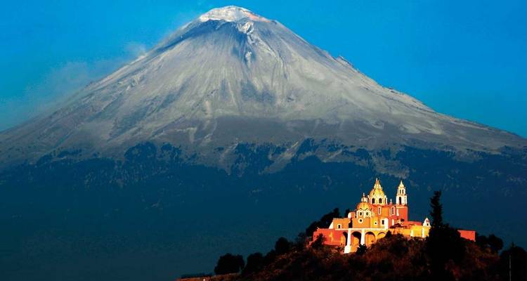 Vista dramática del Volcán Popocatépetl elevándose detrás de la Iglesia de Nuestra Señora de los Remedios en la cima de la colina cerca de Puebla.