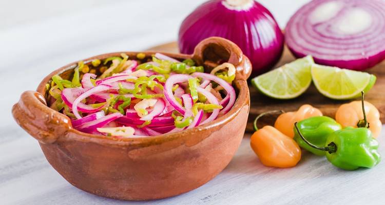 Salsa tradicional de cebolla encurtida de Yucatán servida en un tazón de barro con limas, cebolla morada y chiles habaneros