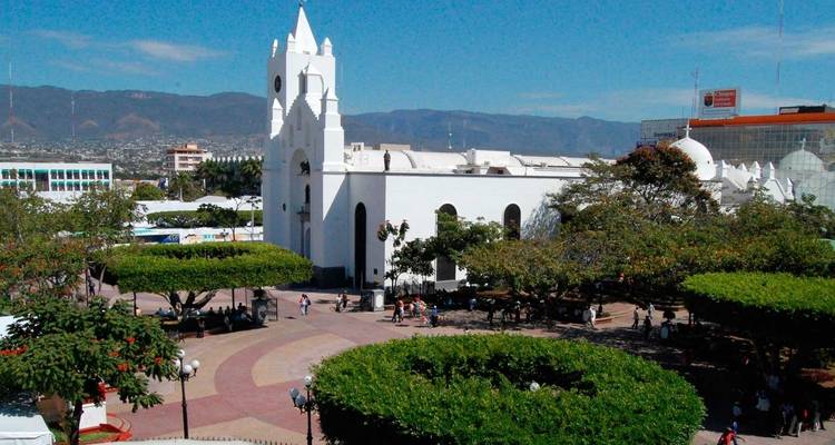 Plaza del pueblo iluminada por el sol con iglesia blanca y árboles bien cuidados, tierras altas mexicanas