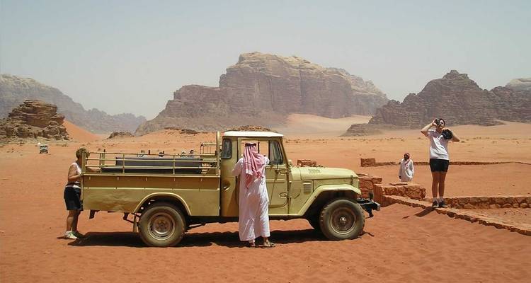 4x4-Jeep und Touristen auf den roten Sandebenen zwischen hoch aufragenden Felsformationen in der Wüste Wadi Rum.