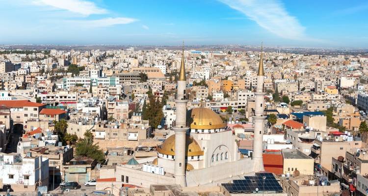 Wide aerial view of Amman’s dense tan buildings and golden-domed mosque beneath a streaked sky.