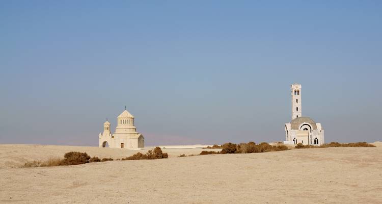 Two small stone shrines standing isolated on a barren sandy plateau beneath a clear blue sky.