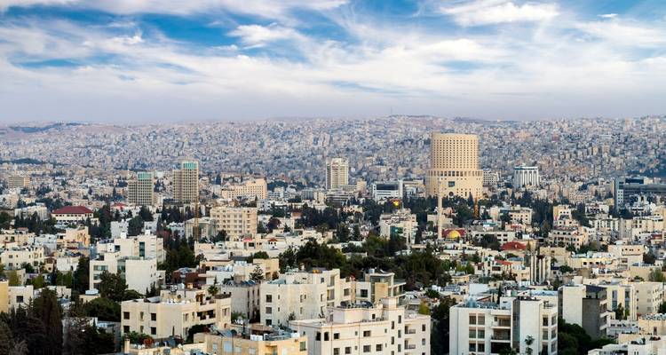 Daytime panorama of a densely packed cityscape stretching across rolling hills beneath streaked clouds.