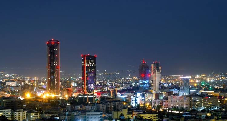Night view over a sprawling city with modern illuminated skyscrapers standing out against the dark sky.