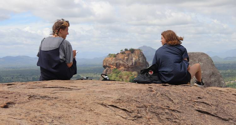 Two people sitting on a rock overlooking Sigiriya Rock.
