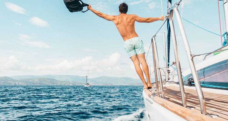 Man leaning off a sailboat over the ocean.