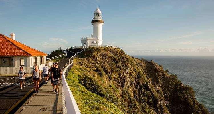 Des personnes marchant près d'un phare sur une falaise au coucher du soleil.