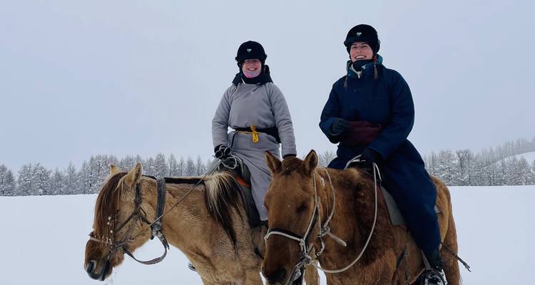 Dos personas vestidas con ropa de invierno montando caballos en un paisaje nevado.