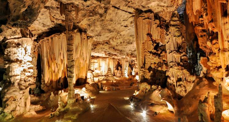 Grotte magnifiquement éclairée avec stalactites et stalagmites.