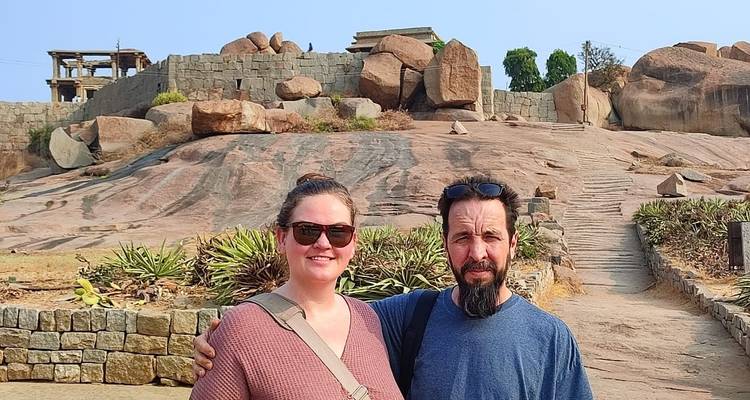 Two people standing on rocky terrain with ancient ruins behind.